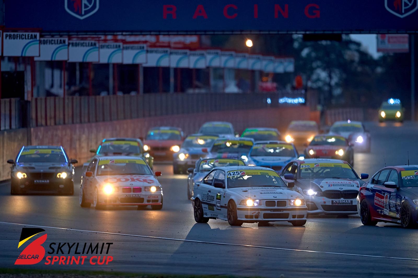 Start eines Rennens im Belcar Skylimit Sprint Cup bei Dämmerung: Mehrere Tourenwagen fahren dicht gedrängt durch die Boxengasse, Scheinwerfer leuchten, im Vordergrund ein BMW mit Startnummer 425. Im Hintergrund sind Boxengebäude und Zuschauerbereiche erkennbar, Rennatmosphäre mit hoher Dynamik.